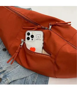 Gros plan sur un sac bandoulière orange avec poches zippées et rangement pour téléphone