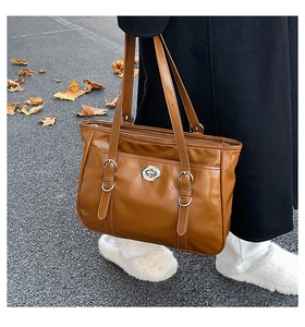 Detail of caramel brown tote bag featuring dual decorative buckles and a metal turn-lock closure
