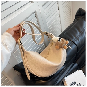 Detail of beige crescent saddle bag in pebble leather with stylish brown plush pendant
