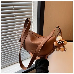 Brown lychee leather crescent shoulder bag with wide strap and plush doll pendant