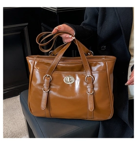 Detail of a brown glossy leather tote bag featuring a silver metal turn-lock and buckle