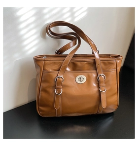 Detailed shot of brown tote bag with decorative metal buckles and silver twist-lock
