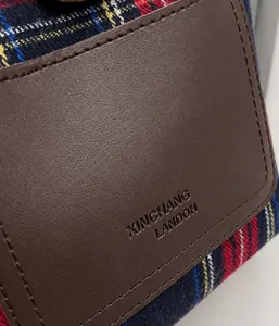 Detail of plaid fabric texture and brown leather flap with embossed brand logo