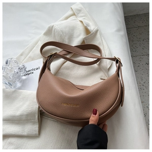 Detail of tan pebble leather crescent bag with gold logo on a white blazer
