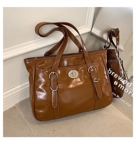 Detail of a brown tote bag with glossy finish and silver turn-lock hardware closure