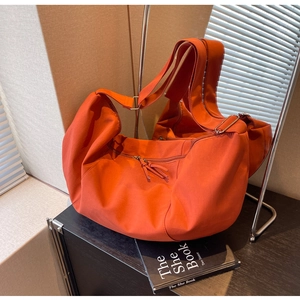 Détail d'un sac cabas en toile orange vif montrant les larges anses et les fermetures éclair