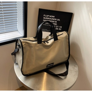 Detail view of the khaki Boston bag with black nylon straps and branding on a metal table