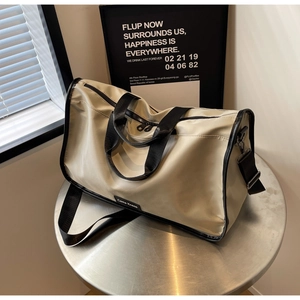 Detail of beige nylon travel duffel bag with black handles on a silver metal table