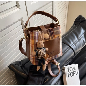 Detail of checkered bucket bag featuring brown leather trim and cute rabbit charm