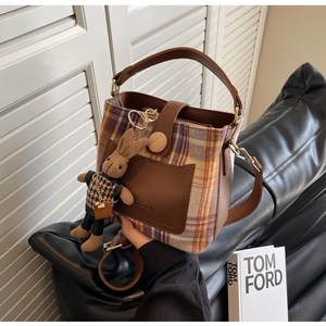 Detail of plaid bucket bag with leather pocket, wooden buckle and plush bunny charm