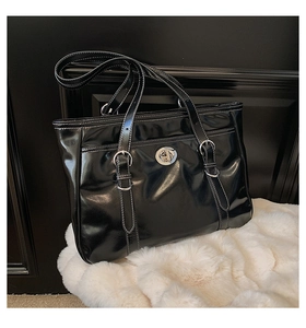 Close-up of black glossy tote bag featuring white contrast stitching and silver turn-lock