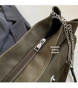 Close-up of smooth silver zipper and chain detail on olive green leather tote bag