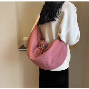 Gros plan d'un sac demi-lune en nylon rose porté à l'épaule par un mannequin en tenue chic