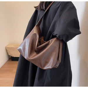 Detailed texture of brown glossy PU leather hobo bag worn by model in black coat