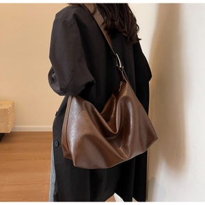 Detail of dark brown leather tote bag showing soft texture and glossy finish on model