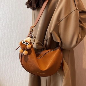Brown leather half-moon crossbody bag with plush charm on a model in trench coat