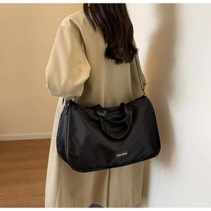Detail showing high-capacity black nylon pillow bag worn by model in a cozy indoor setting