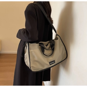 Detail view of khaki nylon tote bag showing wide black shoulder strap and side brand tag