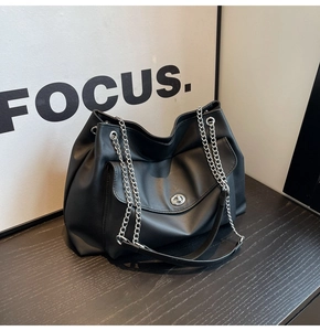 Detail of black faux leather tote bag with silver chain strap and front flap pocket