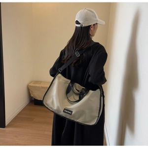 Large beige crossbody pillow bag with wide black straps shown on a model's shoulder