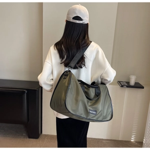 Olive green large nylon travel bag with black straps worn by a model in a cozy interior