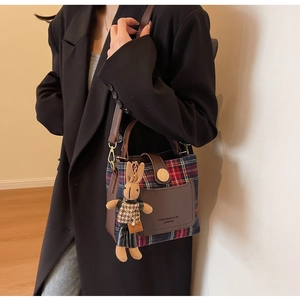 Detail of red plaid bucket bag featuring a plush rabbit pendant and leather strap