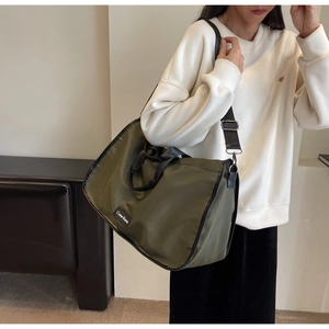 Detail of olive green nylon tote bag featuring black woven straps and brand woven label
