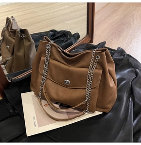 Close-up of caramel brown tote bag with chain strap on black satin fabric texture