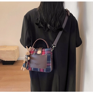 Detail of plaid crossbody bucket bag with leather strap and cute rabbit pendant on a model