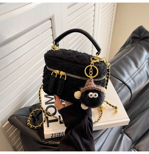 Detail of black tweed handbag with golden chain strap and plush monster charm