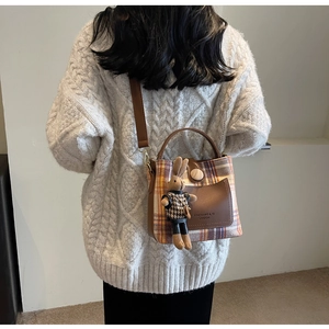 Detail of plaid bucket bag with leather pocket and cute rabbit charm on a knit sweater