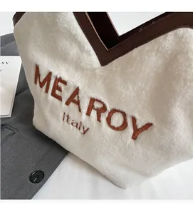 Detail der weißen Plüschtasche mit braunem Ledergriff und gesticktem Logo