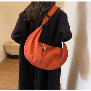 Détail d'un grand sac bandoulière orange en toile de forme croissant avec franges