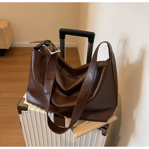 Detail view of large dark brown tote bag with wide strap and silver buckle on suitcase