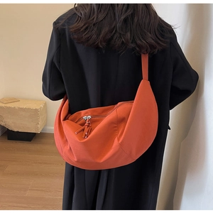 Détail d'un sac demi-lune orange en toile porté sur une personne en manteau noir