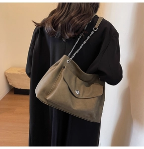 Detail of suede tote bag with metal chain strap and twist lock closure on a model