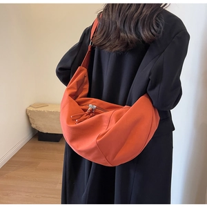 Grand sac bandoulière orange porté par un mannequin, détail de sangle large et gland
