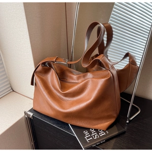 Detail of brown leather tote bag showing grainy texture and wide adjustable shoulder strap