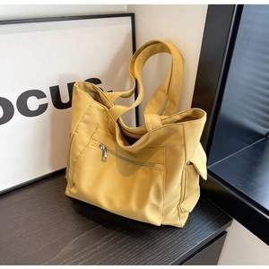 Detail of yellow canvas tote bag featuring front zipper pocket and side flap compartment