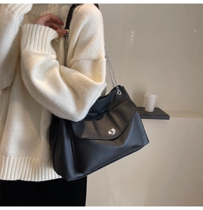 Detail of a large black shoulder bag with silver chain strap and metal swivel lock buckle