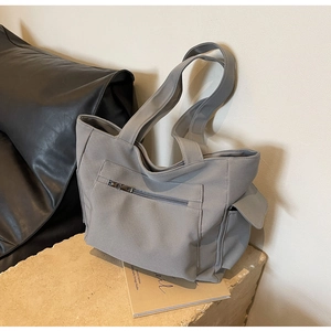 Detail of grey canvas tote bag featuring front zipper pocket and side flap compartment