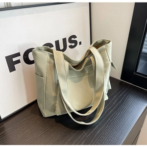 Detail view of a sage green canvas tote bag featuring a front zipper and side pocket