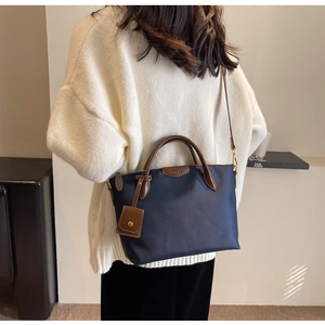 Detail of navy nylon tote bag with brown leather handles worn by a model in a knit sweater