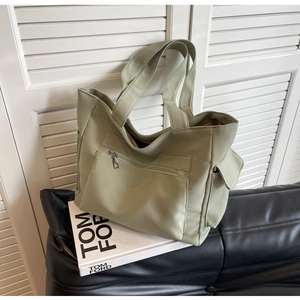 Detail view of sage green canvas tote bag with side utility pocket on leather bench