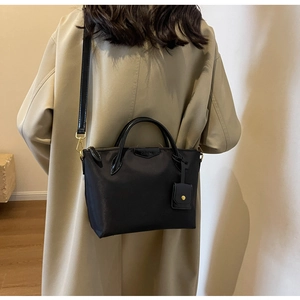Detailed view of black nylon tote with leather handles on a trench coat model
