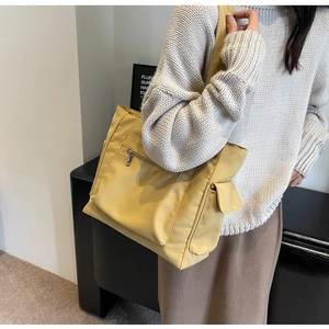 Detail of yellow canvas tote bag showing metal zipper pocket and side flap compartment