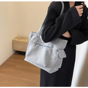 Detail of light grey nylon tote bag featuring front zip pocket and side flap compartment