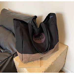Détail du sac cabas en toile montrant le contraste du tissu noir et le fond en daim brun