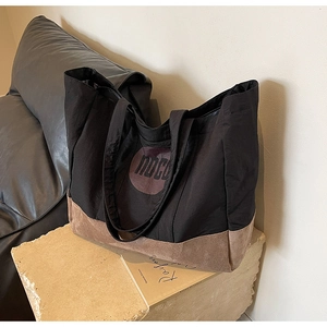 Gros plan du sac cabas en toile noire avec base en daim marron et logo IDCD sur pierre