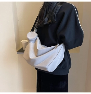 Détail du sac bandoulière gris clair avec un porte-monnaie rond suspendu à la sangle